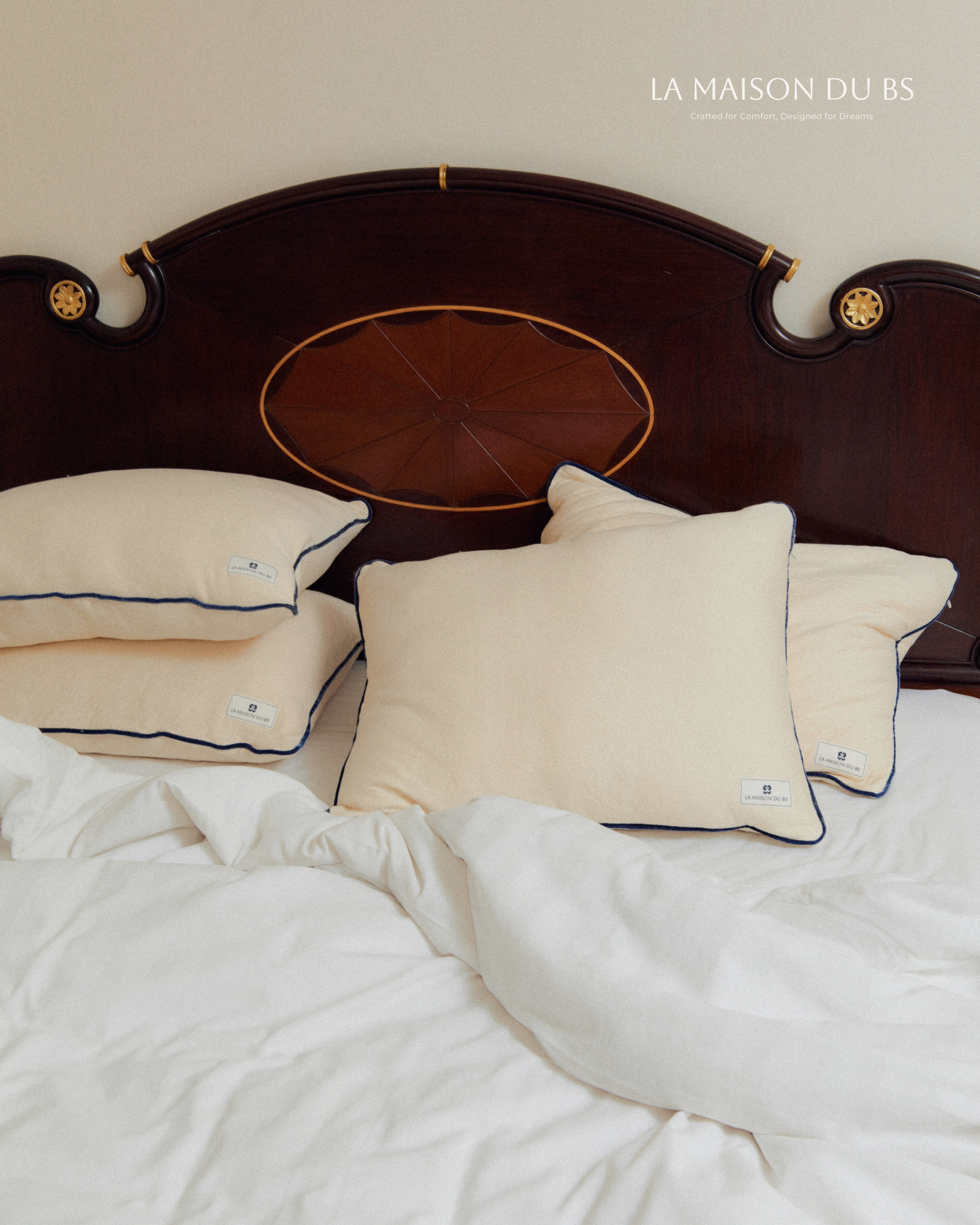 หมอนออร์แกนิก La Maison du BS จัดวางหลายใบบนเตียงไม้สีน้ำตาลคลาสสิก บ่งบอกถึงความหรูหราและความสบาย เหมาะสำหรับการนอนหลับอย่างมีคุณภาพ