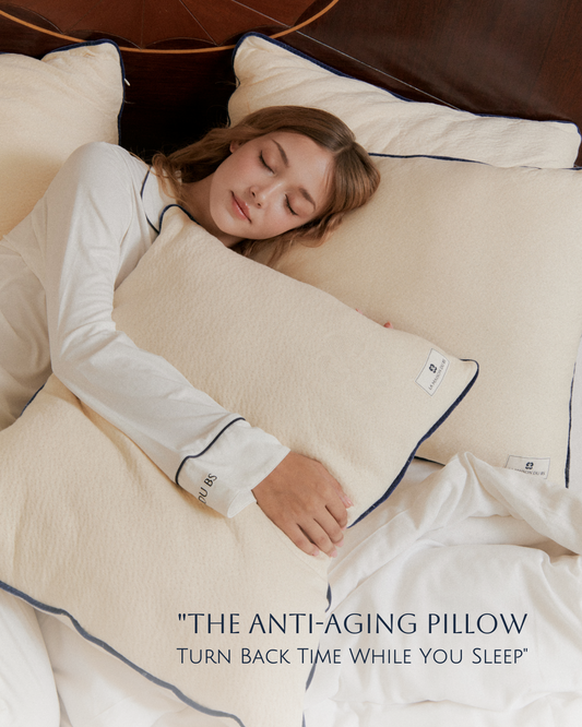 ผู้หญิงนอนกอดหมอนออร์แกนิก La Maison du BS หลับอย่างสบายบนเตียง พร้อมข้อความ The Anti-Aging Pillow – Turn Back Time While You Sleep หมอนเพื่อสุขภาพที่ช่วยลดแรงกดทับและถนอมผิว
